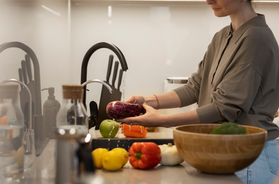 Person rinsing eggplant and other fresh vegetables under running water to practice safe food handling.