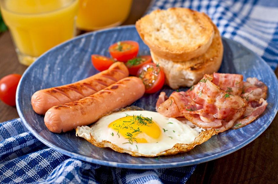 Global breakfast ideas featuring a Western-style plate with fried egg, grilled sausages, crispy bacon, toast, and orange juice.