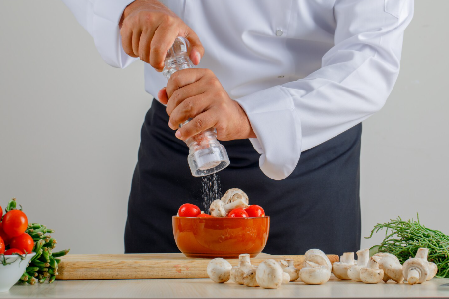 Chef sprinkling salt over a bowl of tomatoes and mushrooms, illustrating how to fix over-salted dishes.