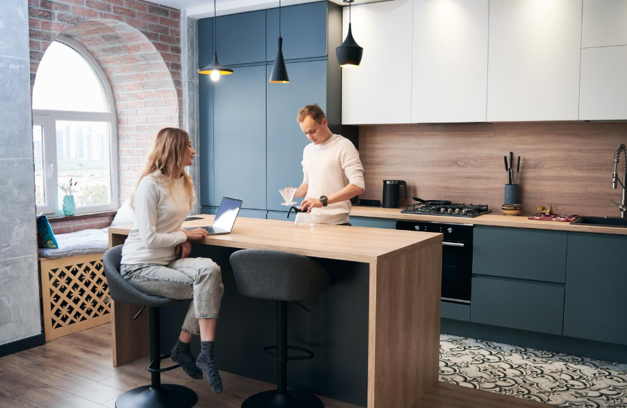 Modern 2025 kitchen design with wood island, blue cabinetry, and couple chatting while making coffee.