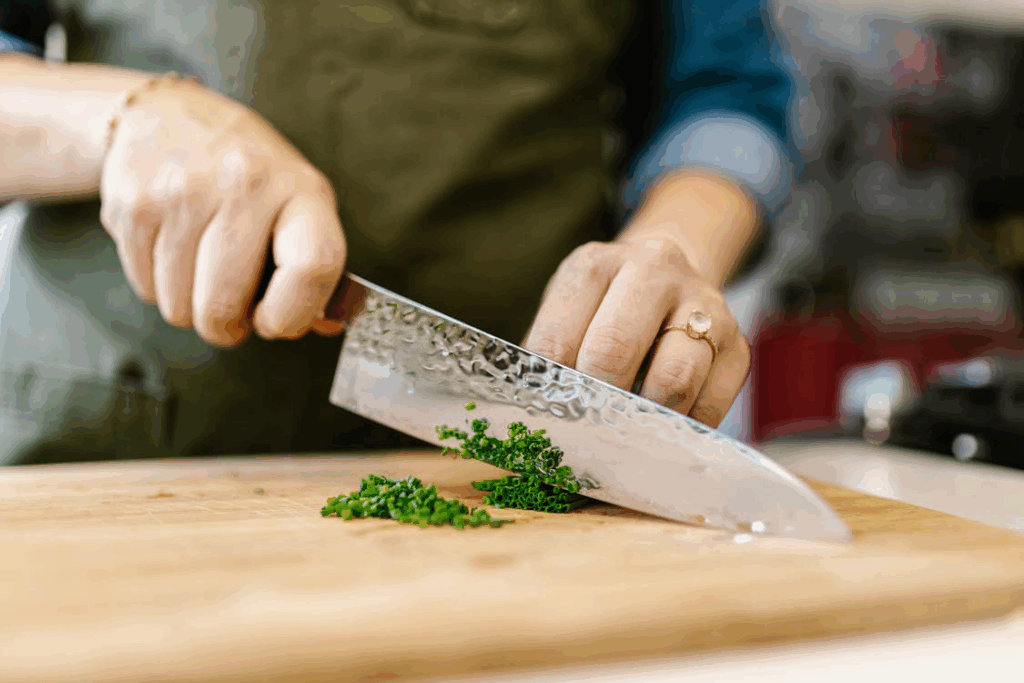 Home cook practicing knife skills, finely chopping fresh herbs on a wooden cutting board.