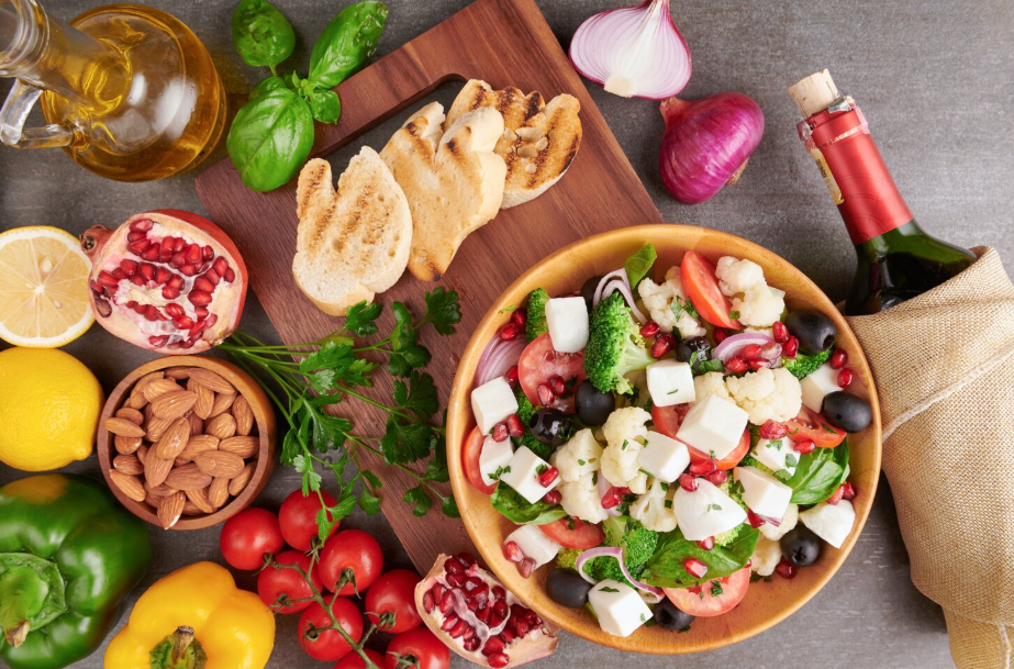 Overhead view of a Mediterranean salad with feta, olives, tomatoes, surrounded by pantry staples like olive oil.