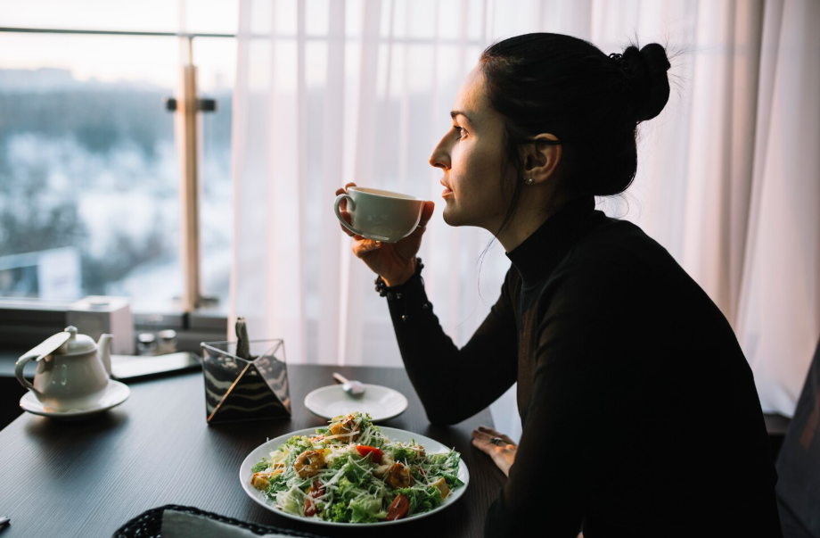 Woman drinking tea and pausing before eating a fresh salad, practicing mindful eating.