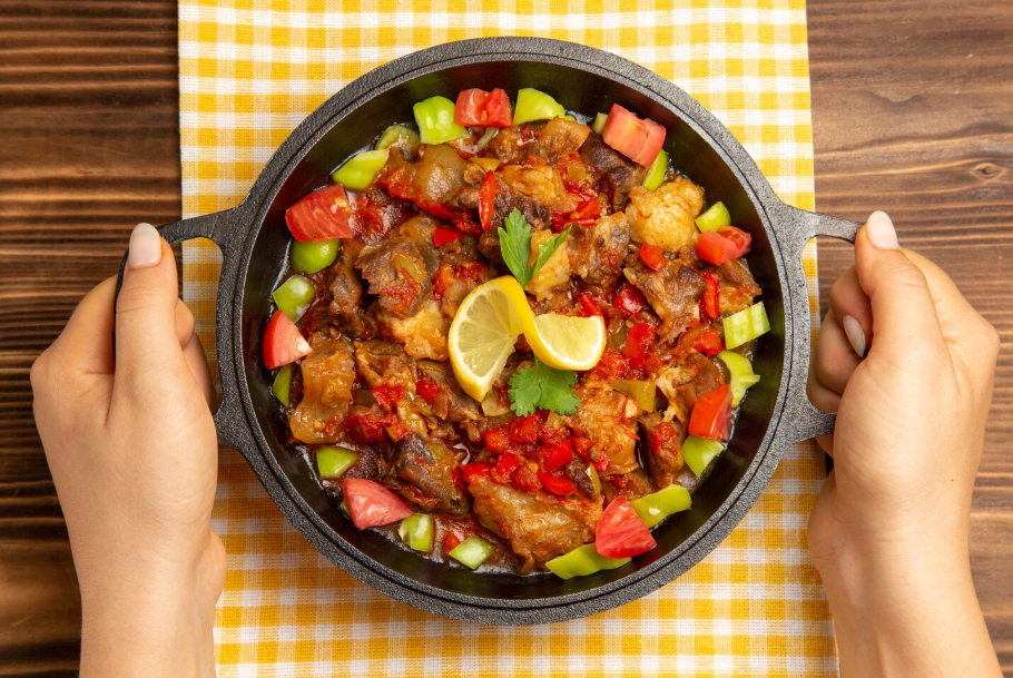 Overview of a cooked vegetable meal with meat, peppers, and a garnish of sliced lemons.