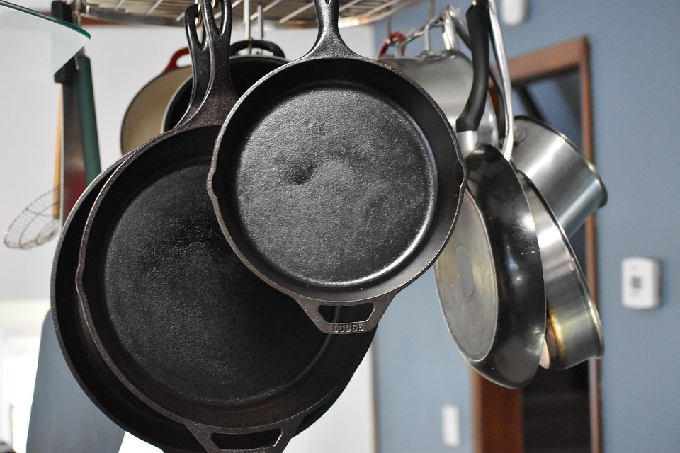 Close-up of seasoned cast iron skillets hanging from a kitchen rack, ready for cooking.