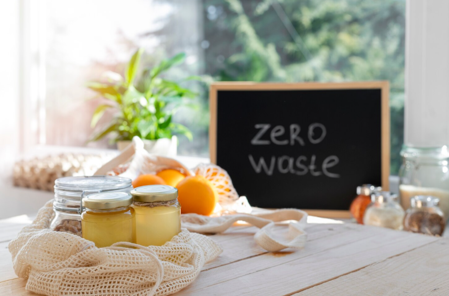 Glass jars, oranges, and reusable produce bags arranged on a wooden counter, illustrating “zero waste” kitchen.