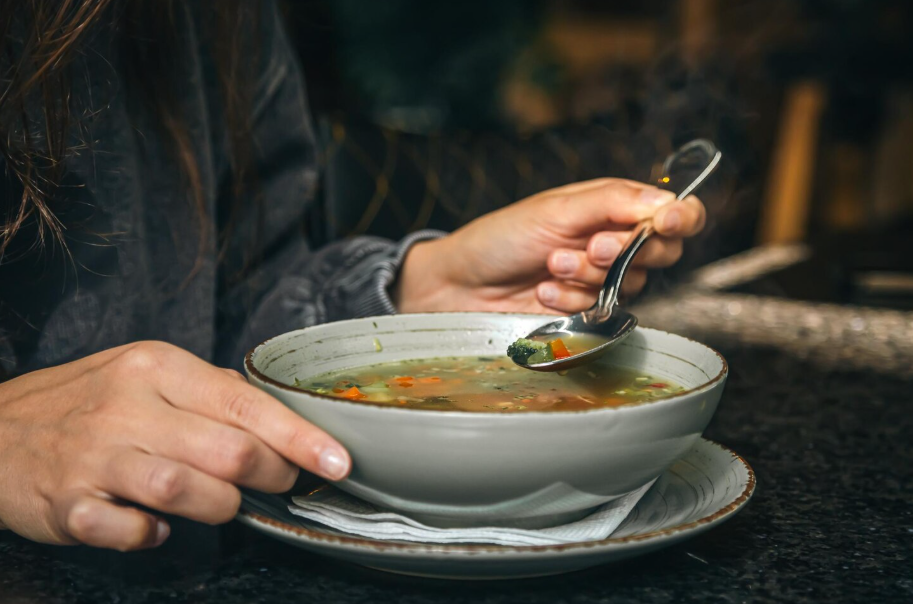 Close-up of a person holding a steaming bowl of vegetable soup, capturing the comfort of a homemade meal.
