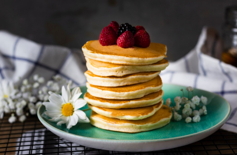 Tall stack of golden, fluffy pancakes with fresh berries, styled with flowers for a cozy breakfast scene.