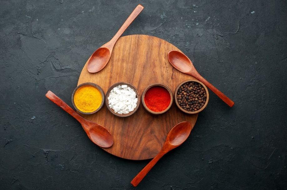 Top view of four small bowls filled with yellow turmeric, coarse salt, red chili powder, and black peppercorns.