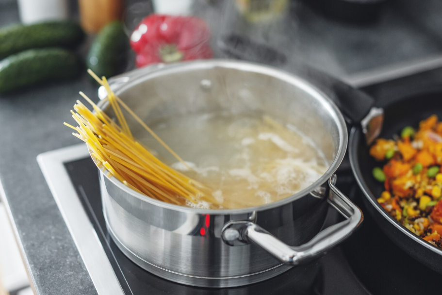 Uncooked spaghetti softening in a large pot of boiling salted water on the stove.