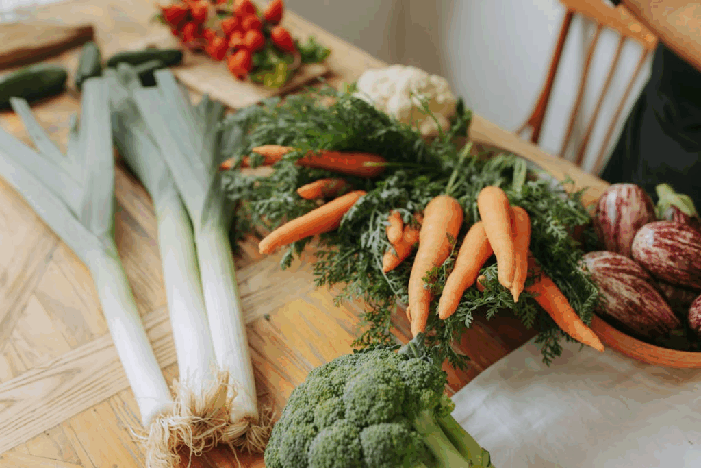 Assorted seasonal vegetables including leeks, carrots, broccoli, and eggplants arranged on a wooden table.