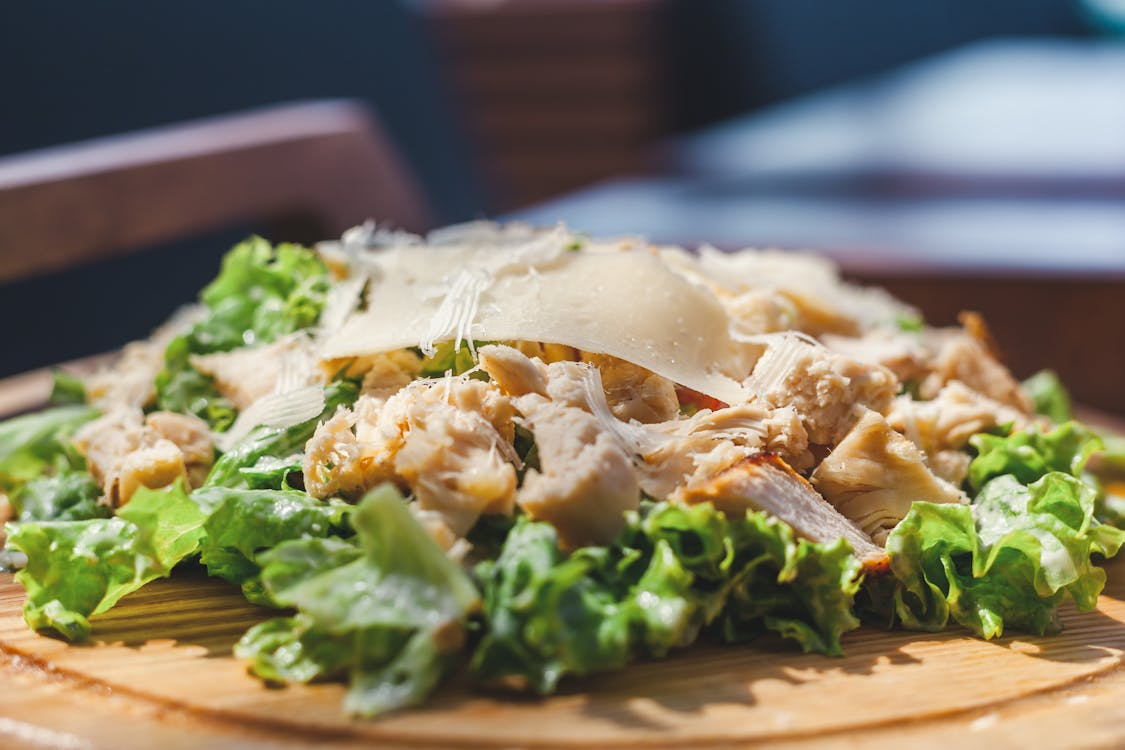 Leftover chicken recipes salad with shredded chicken, crisp lettuce, and shaved cheese on a wooden plate.
